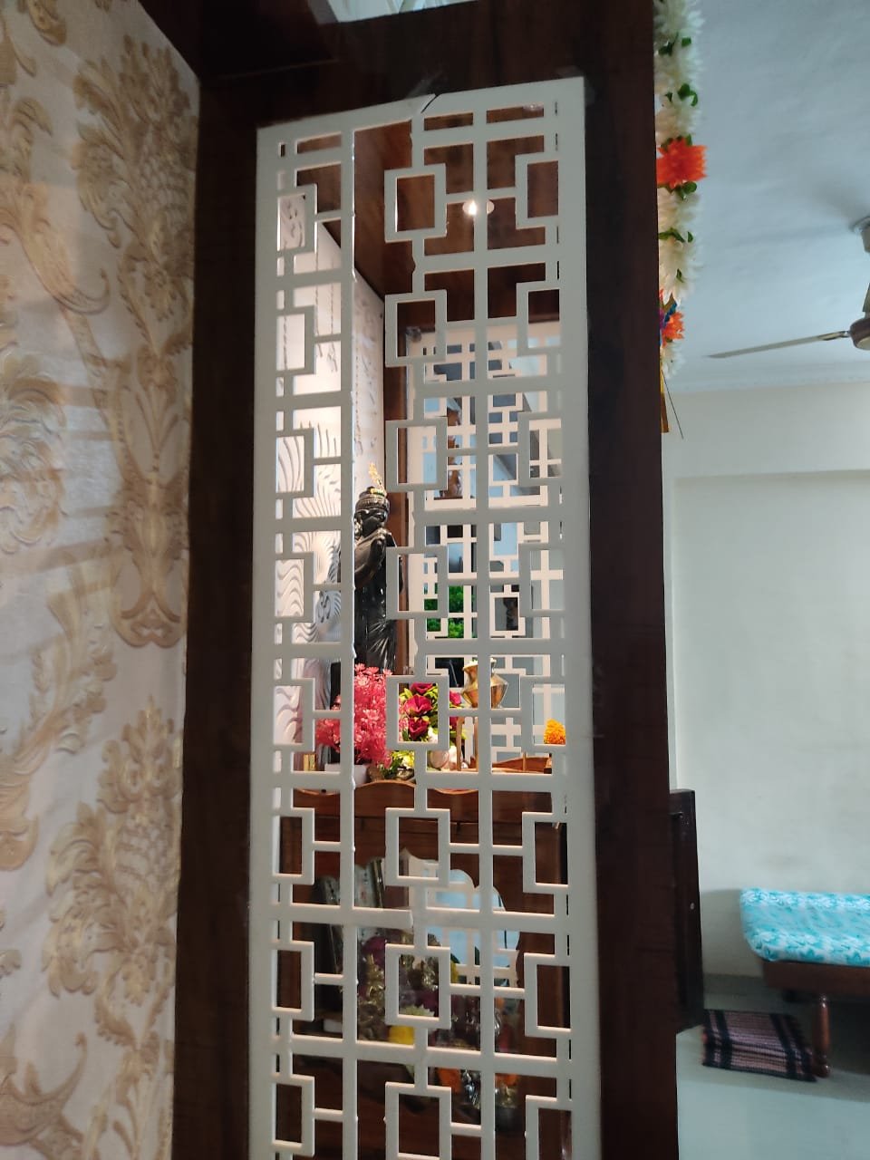 Decorative acrylic jali partition with square-grid design placed near a home pooja setup