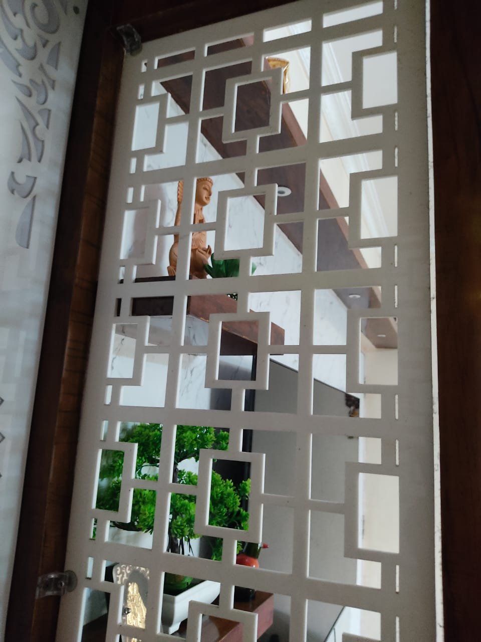 Acrylic jali partition with geometric cut-outs installed beside a pooja room
