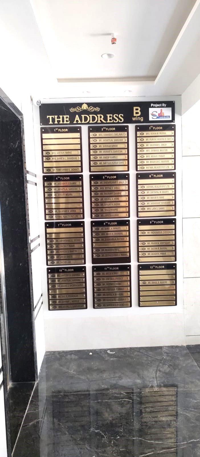 High-rise housing society name board for The Address B Wing listing 12 floors.