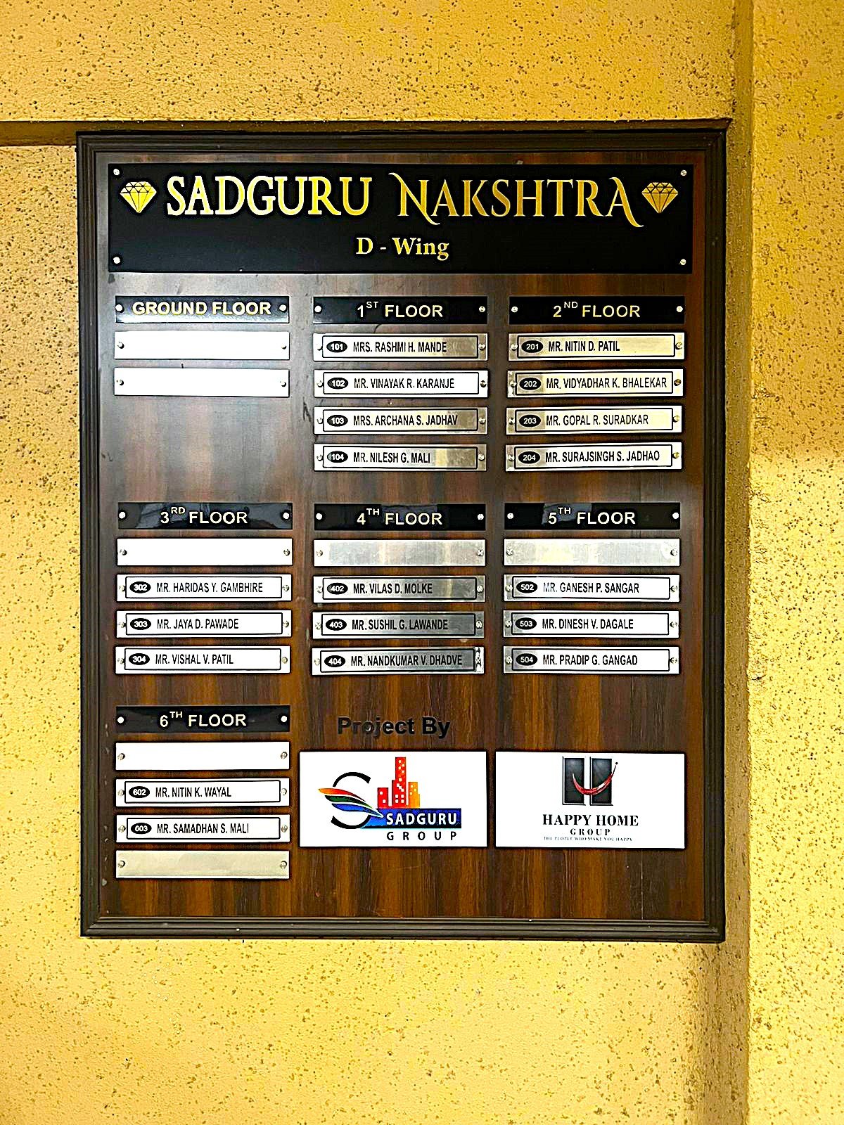 Wood finish housing society name board for Sadguru Nakshatra D Wing with white slats.